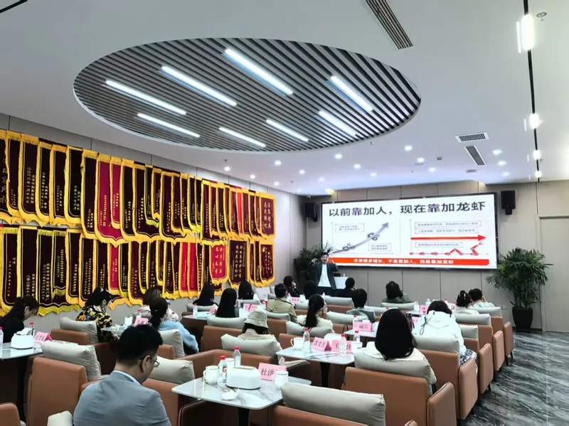 企业内训现场，左侧整面墙挂满客户送的锦旗，大屏是「以前靠加人，现在靠加龙虾」